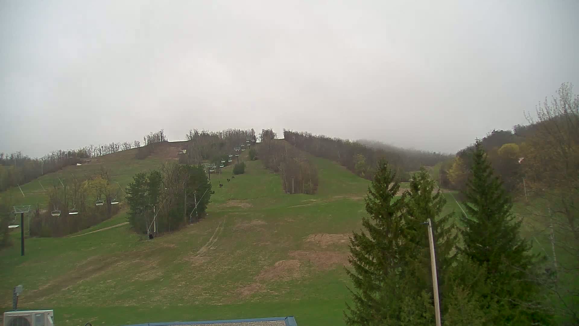 A grassy ski slope with chairlifts is visible under an overcast sky.