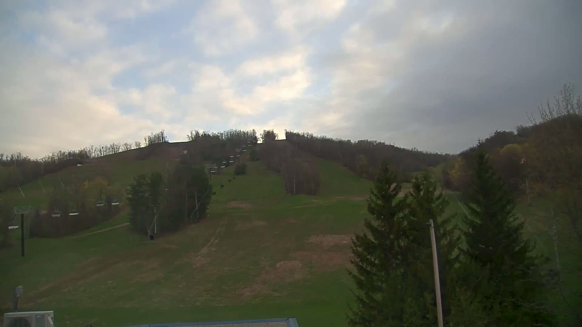 A grassy hillside with a ski lift and sparsely wooded areas is visible under a cloudy sky.