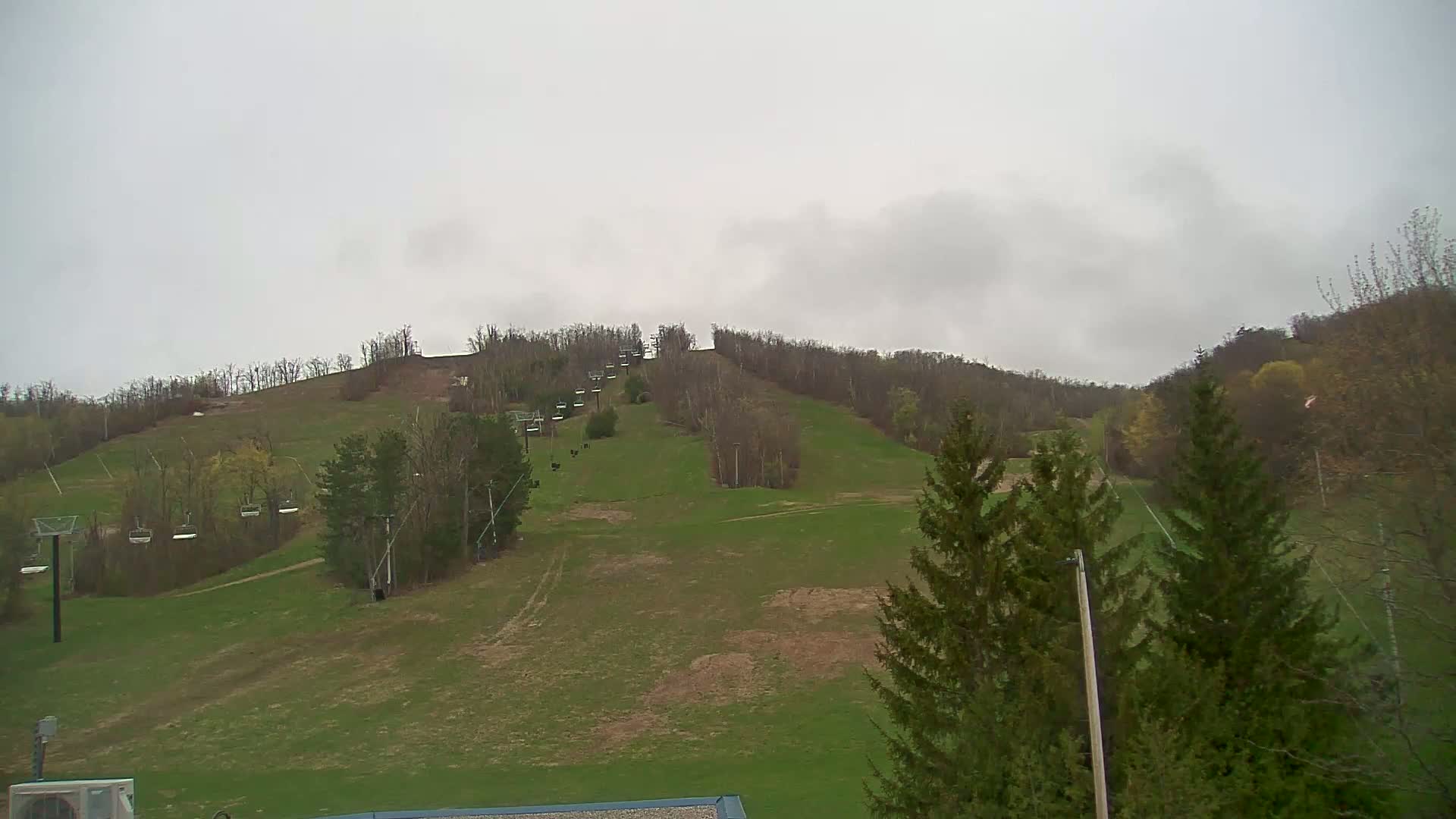 A grassy ski slope with several chairlifts is visible under an overcast sky.