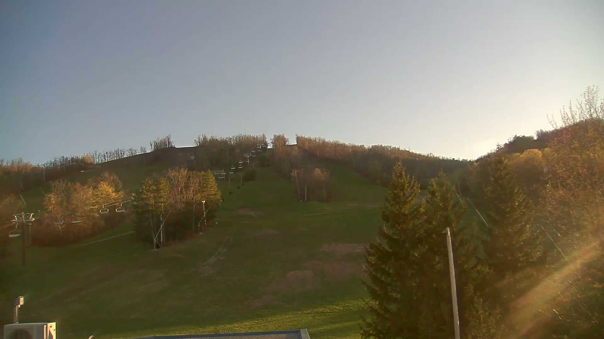 A grassy hillside with a chairlift and scattered trees under a clear, bright sky.