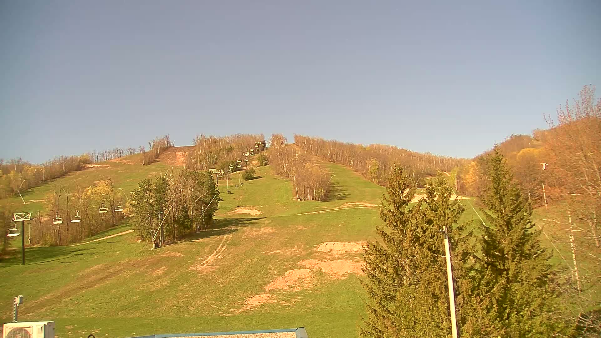 A grassy ski slope with chairlifts and sparse trees under a clear, bright sky.