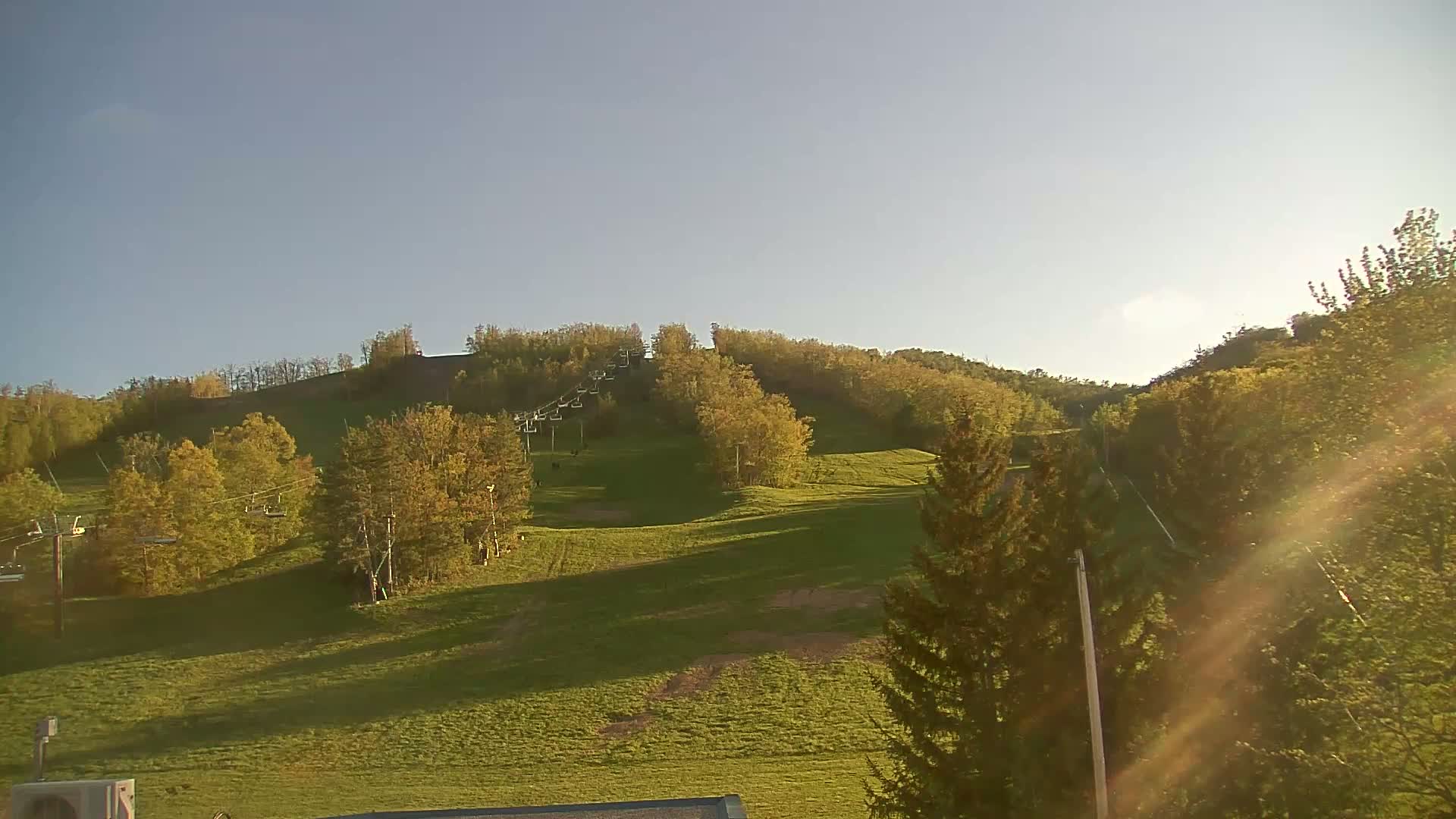 A grassy hill with a chairlift and trees under a clear, bright sky.