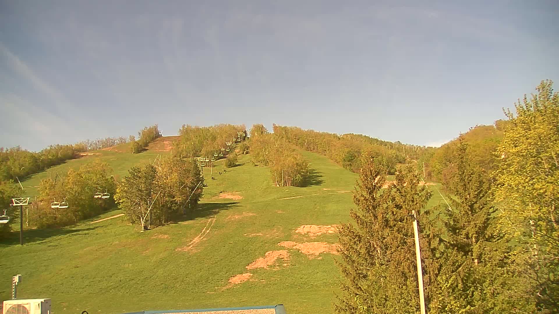 A grassy hillside with a chairlift and budding deciduous trees under a clear blue sky.