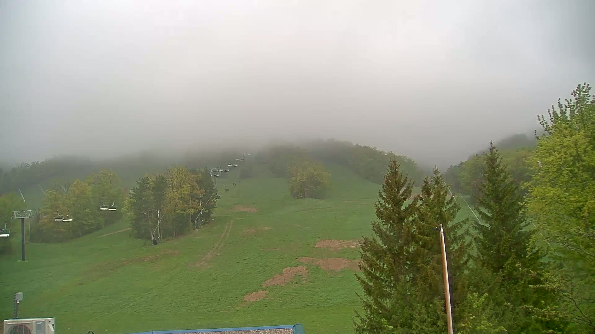 A foggy, grassy hillside with a chairlift and several evergreen trees is visible.