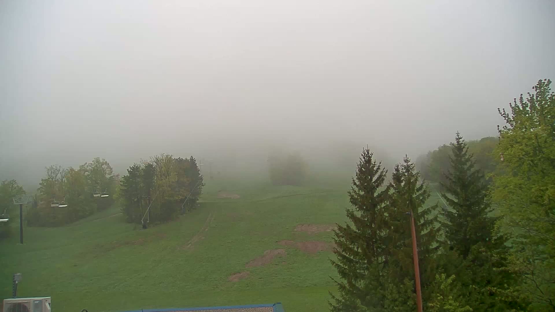A foggy, grassy field with trees and ski lift infrastructure is visible in the distance.