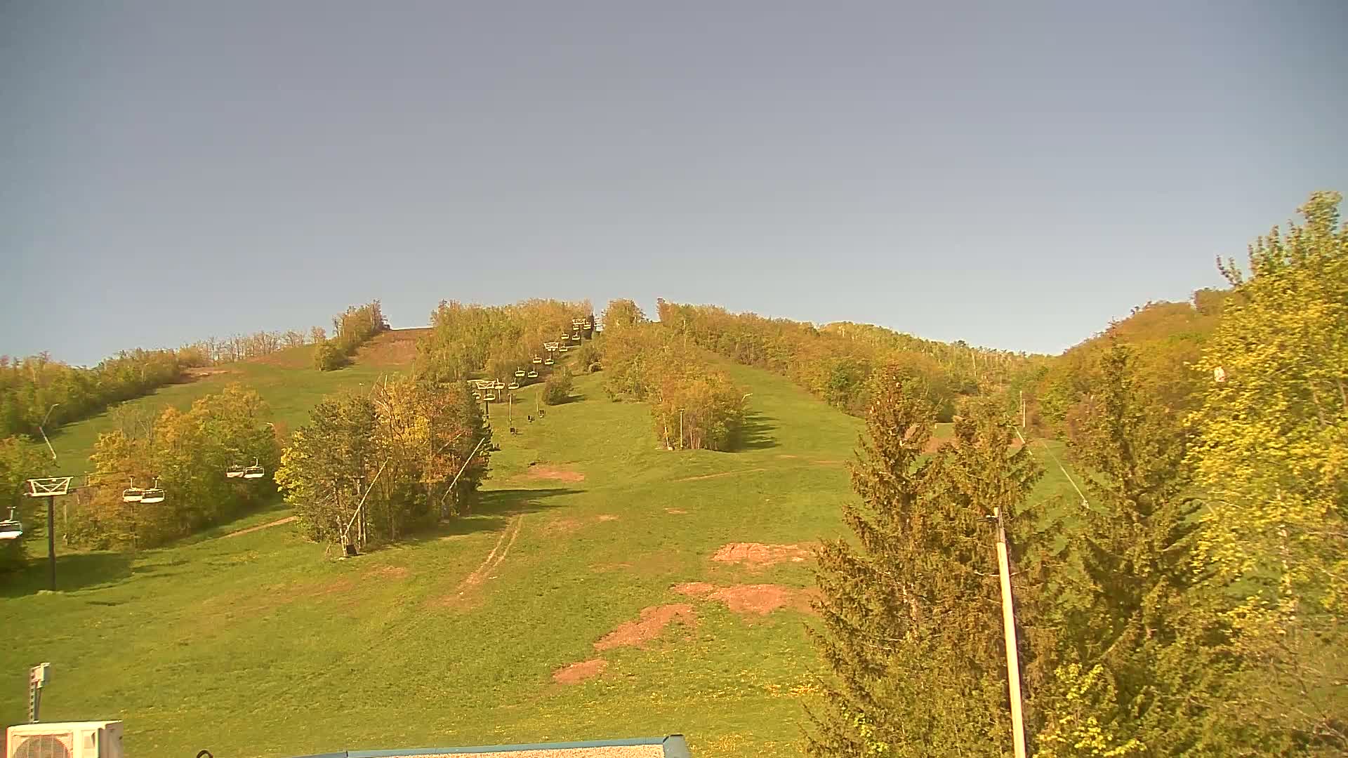 A grassy hill with a chairlift running up its length, surrounded by trees under a clear sky.