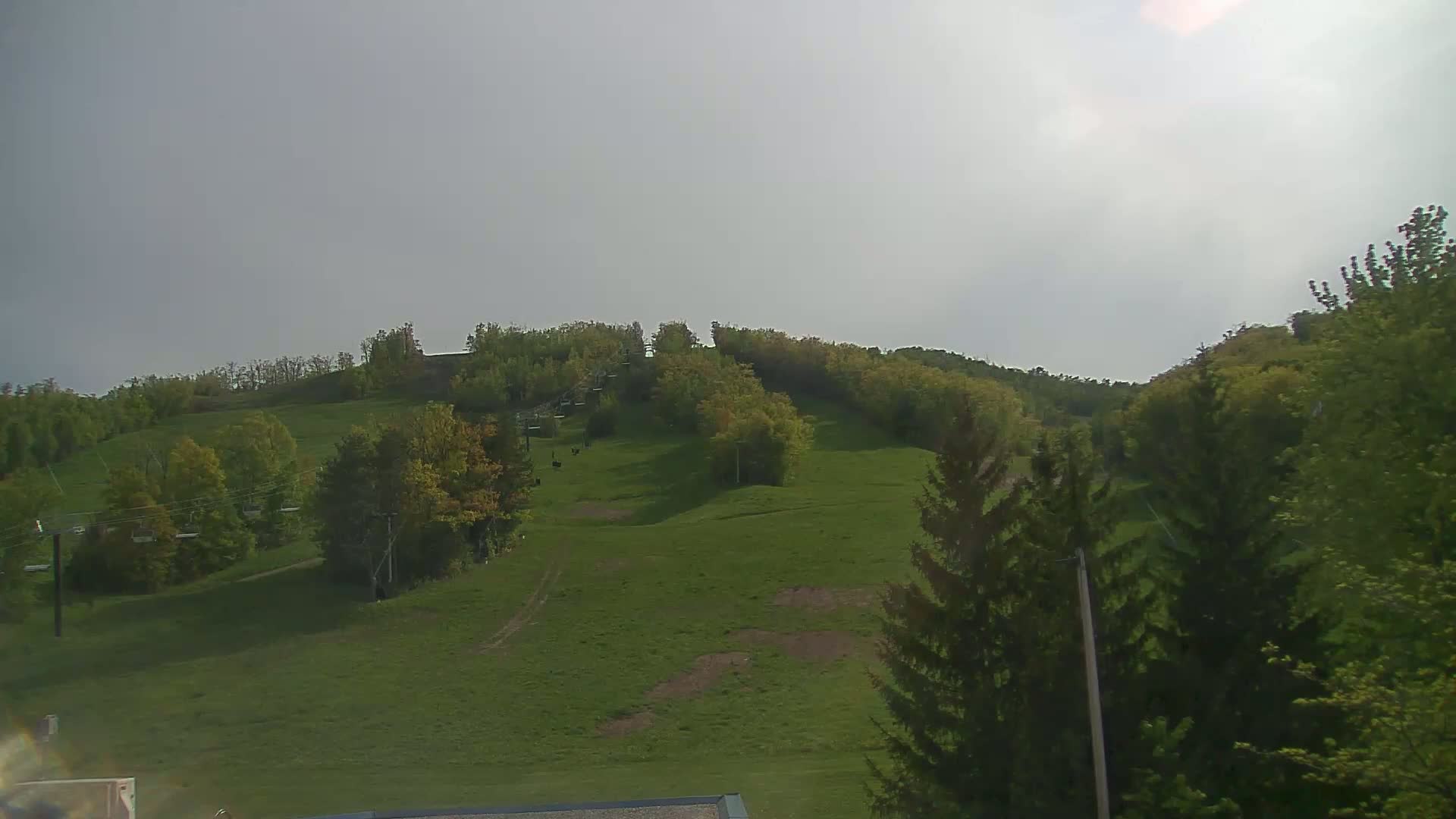 A grassy hill with trees and a chairlift under a cloudy sky.