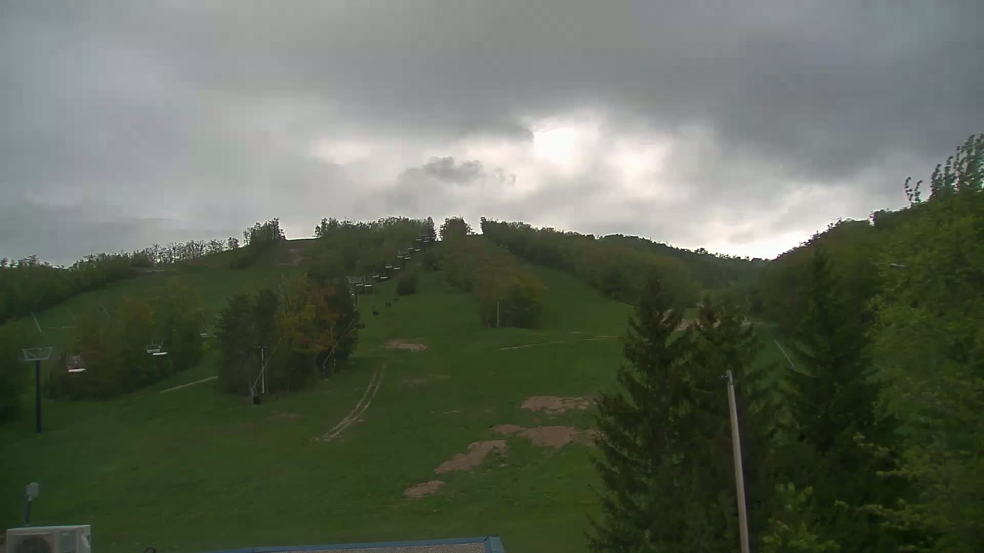 A grassy hillside with a chairlift and trees under an overcast sky.