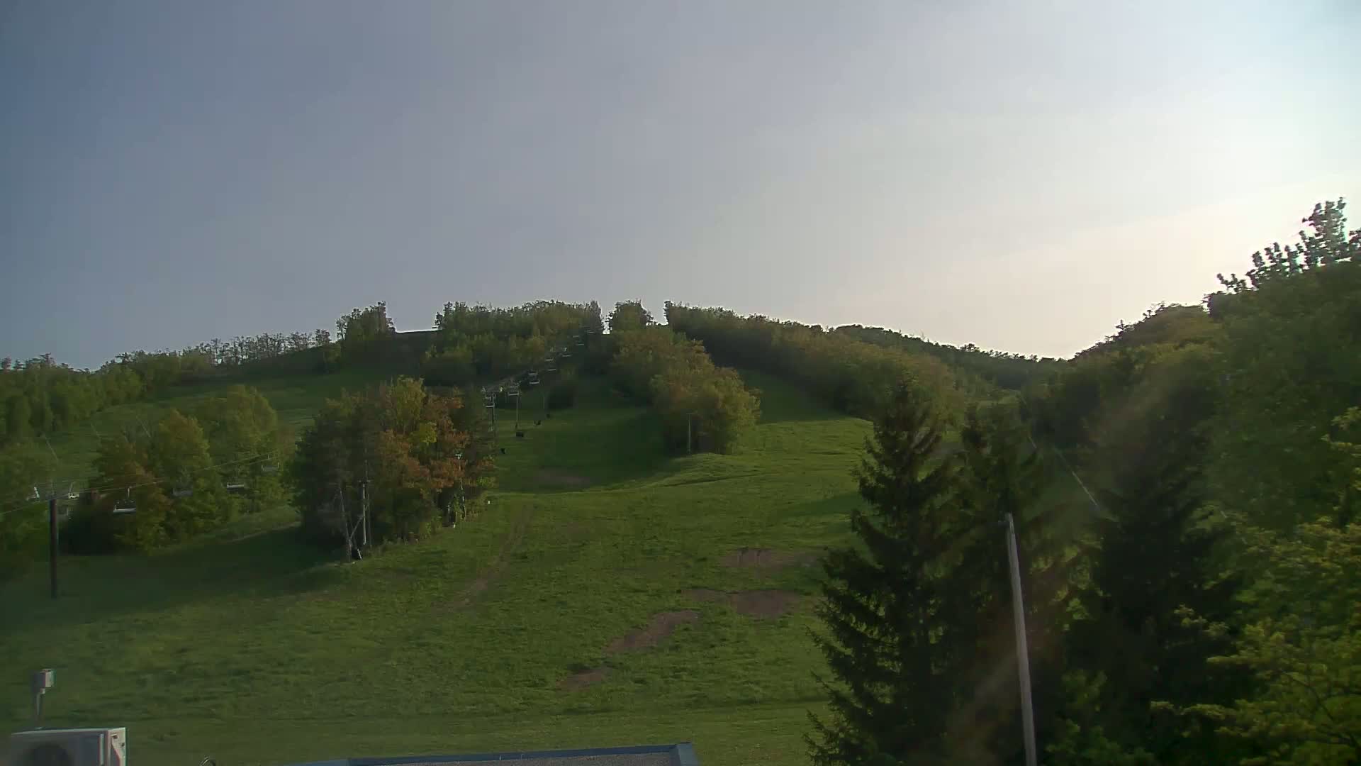 A grassy hill with trees and a chairlift is visible under a clear, bright sky.