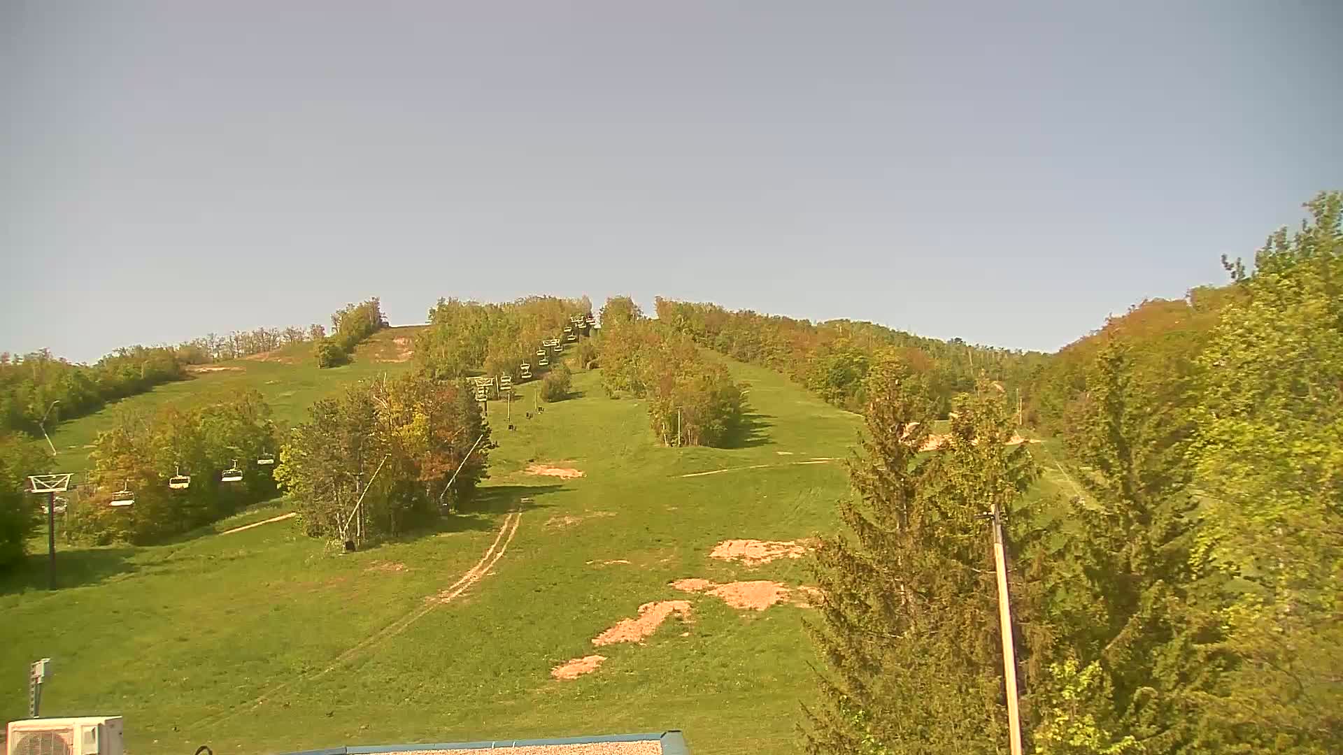 A grassy hillside with a chairlift and trees under a clear sky.