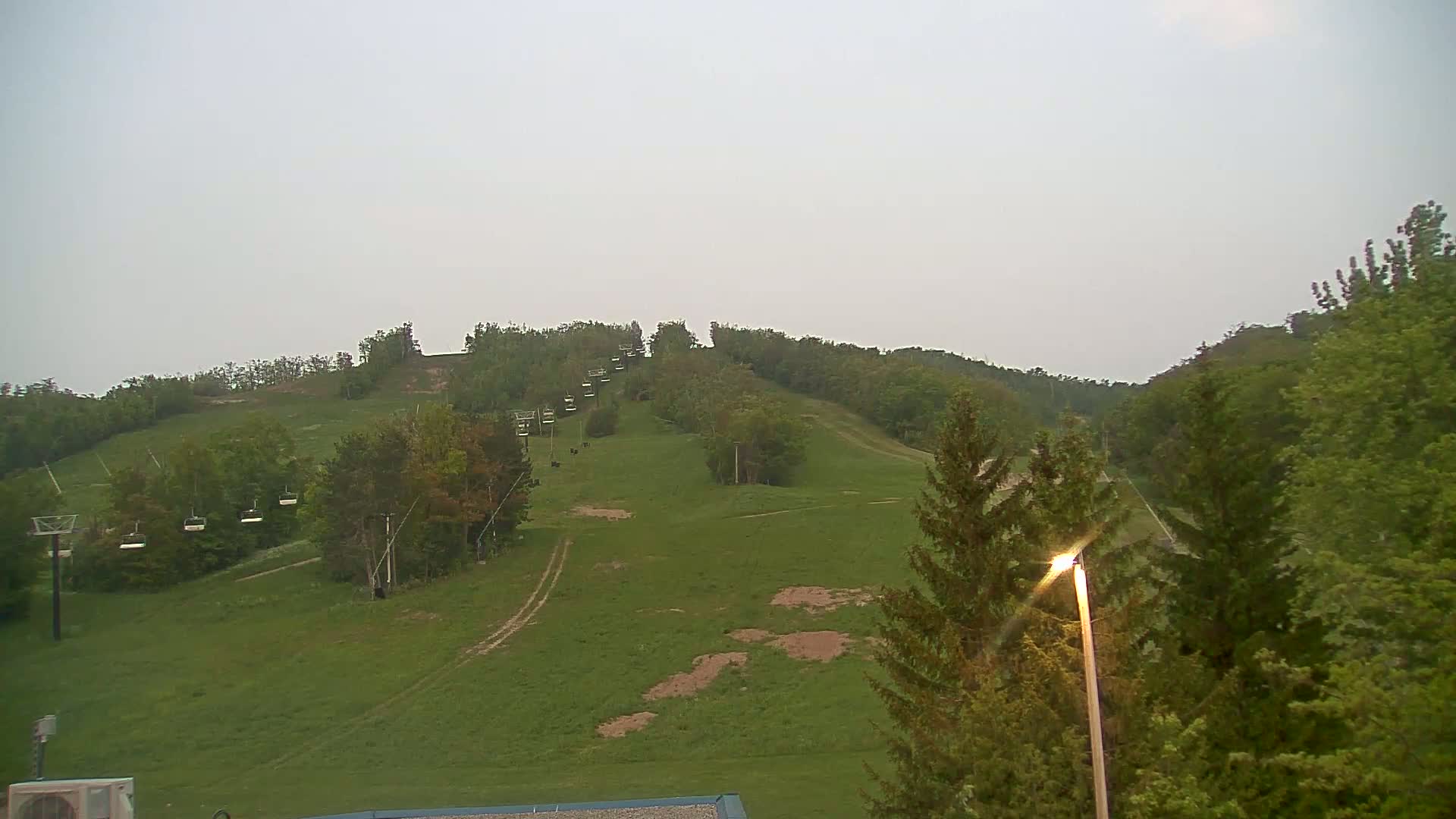 A grassy hillside with a chairlift and trees under an overcast sky.