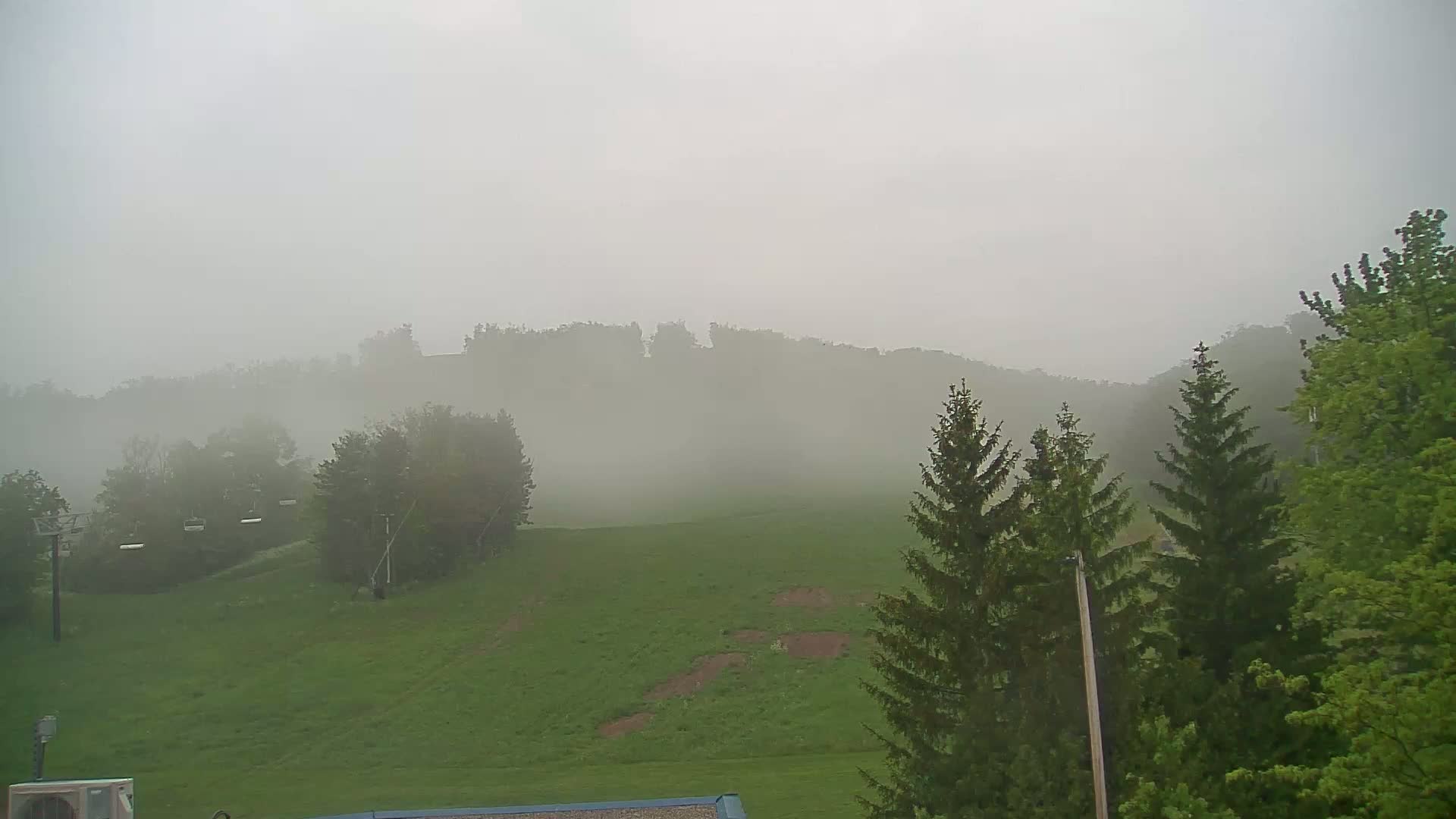 A foggy, green hillside with trees and a chairlift is visible in the distance.
