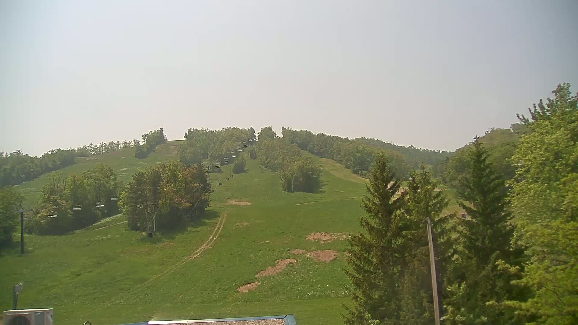 A grassy hill with a chairlift and trees under a hazy sky.