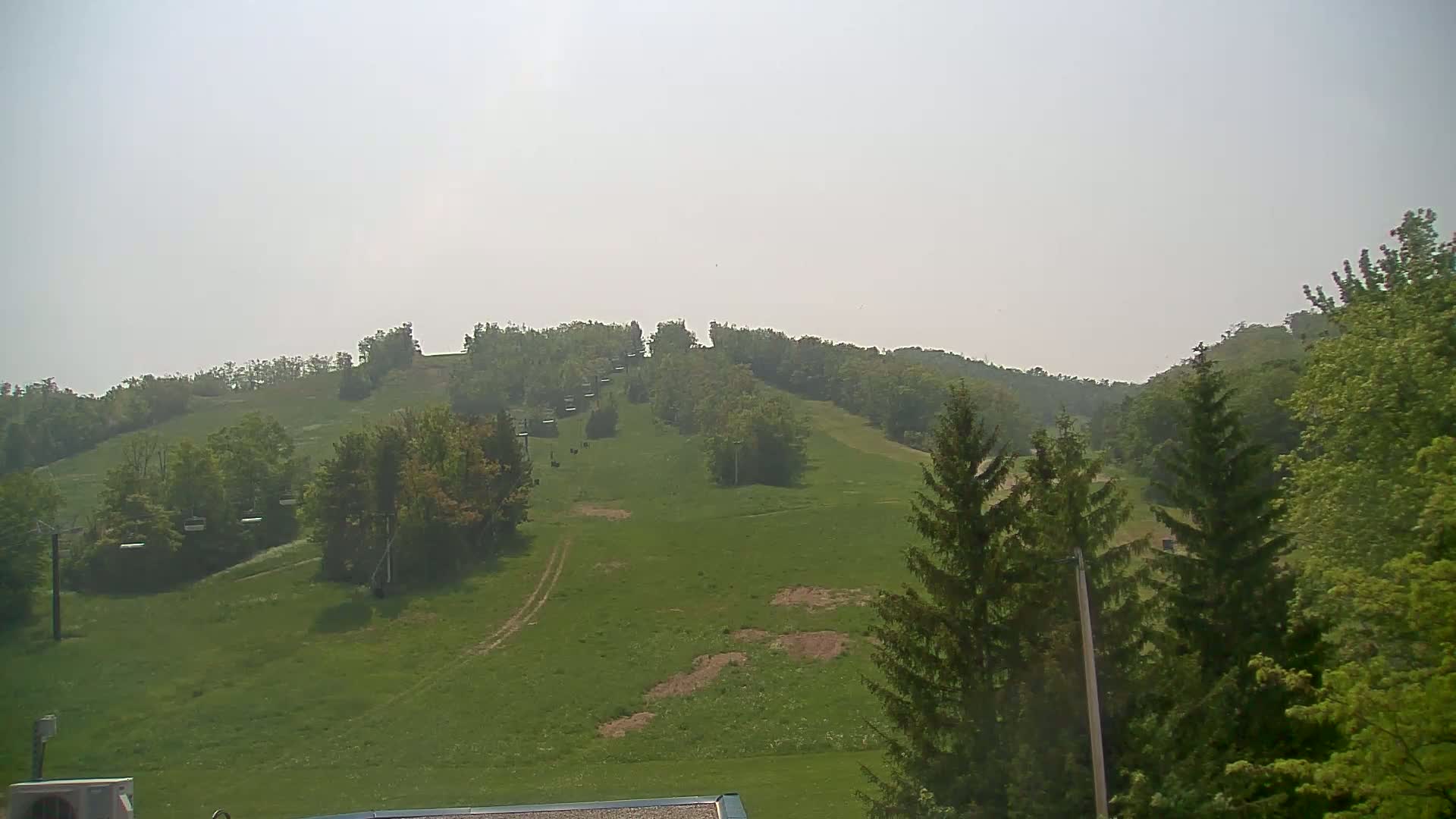 A grassy hillside with a chairlift and trees under a hazy sky.