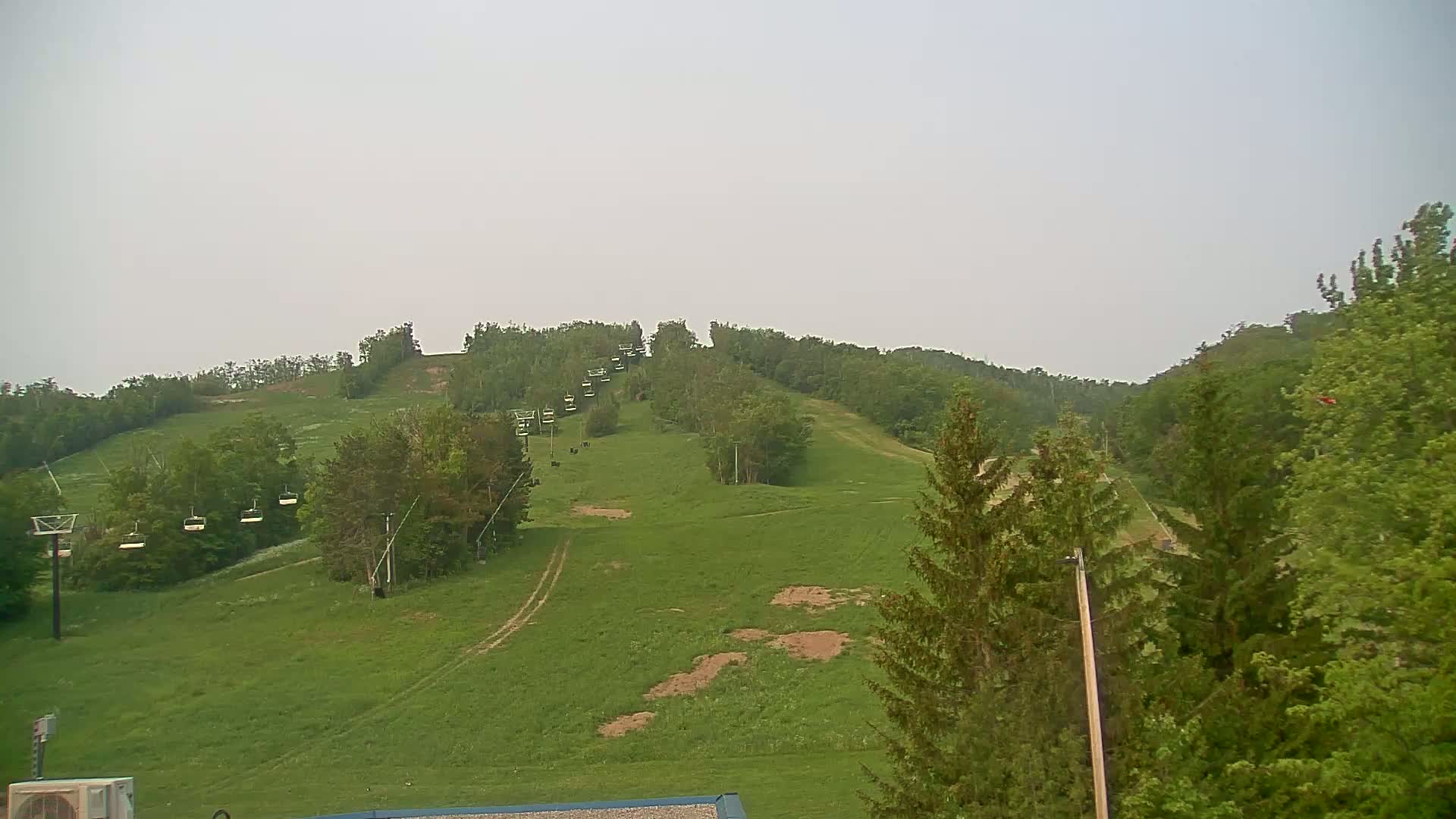 A grassy hillside with a chairlift and several trees is visible under an overcast sky.