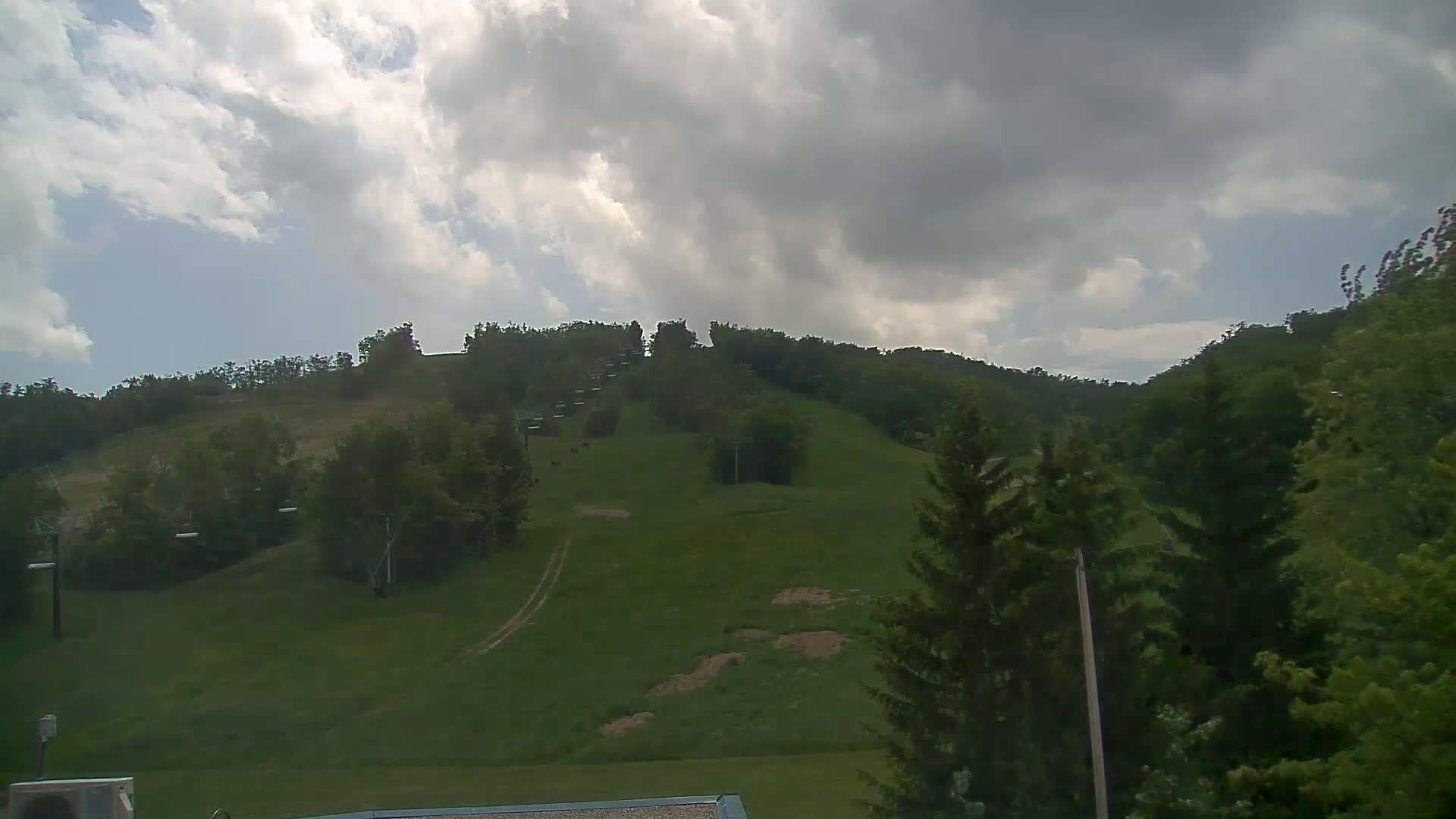 A grassy hill with a chairlift and trees under a partly cloudy sky.