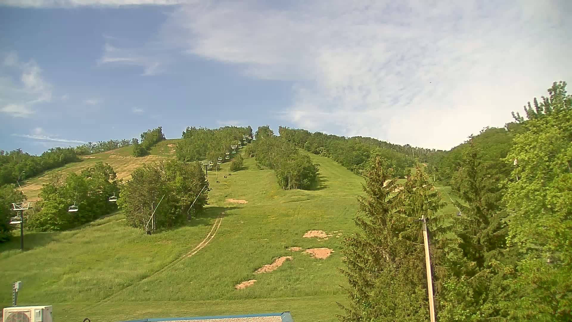 A grassy hill dotted with trees and a chairlift ascends under a partly cloudy sky.