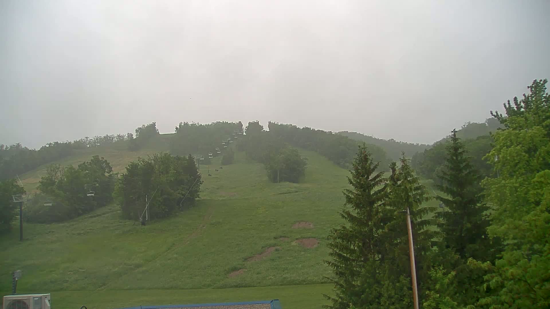 A grassy hillside with a chairlift and trees is visible in the hazy, rainy weather.