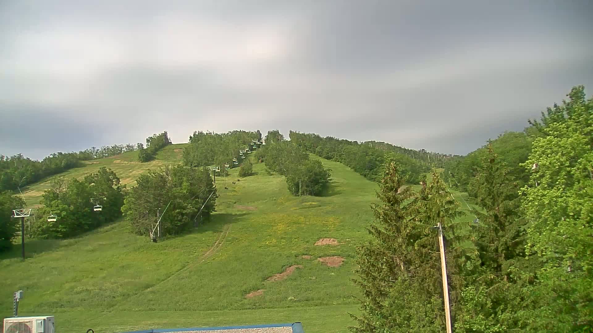 A grassy hill, dotted with trees and a chairlift, stretches upward under a cloudy sky.