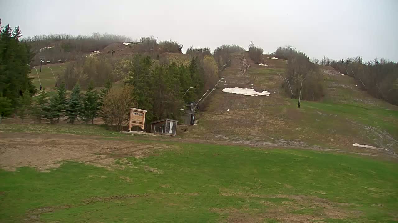 A mostly grassy ski hill with a chairlift and small outbuildings is visible under an overcast sky.