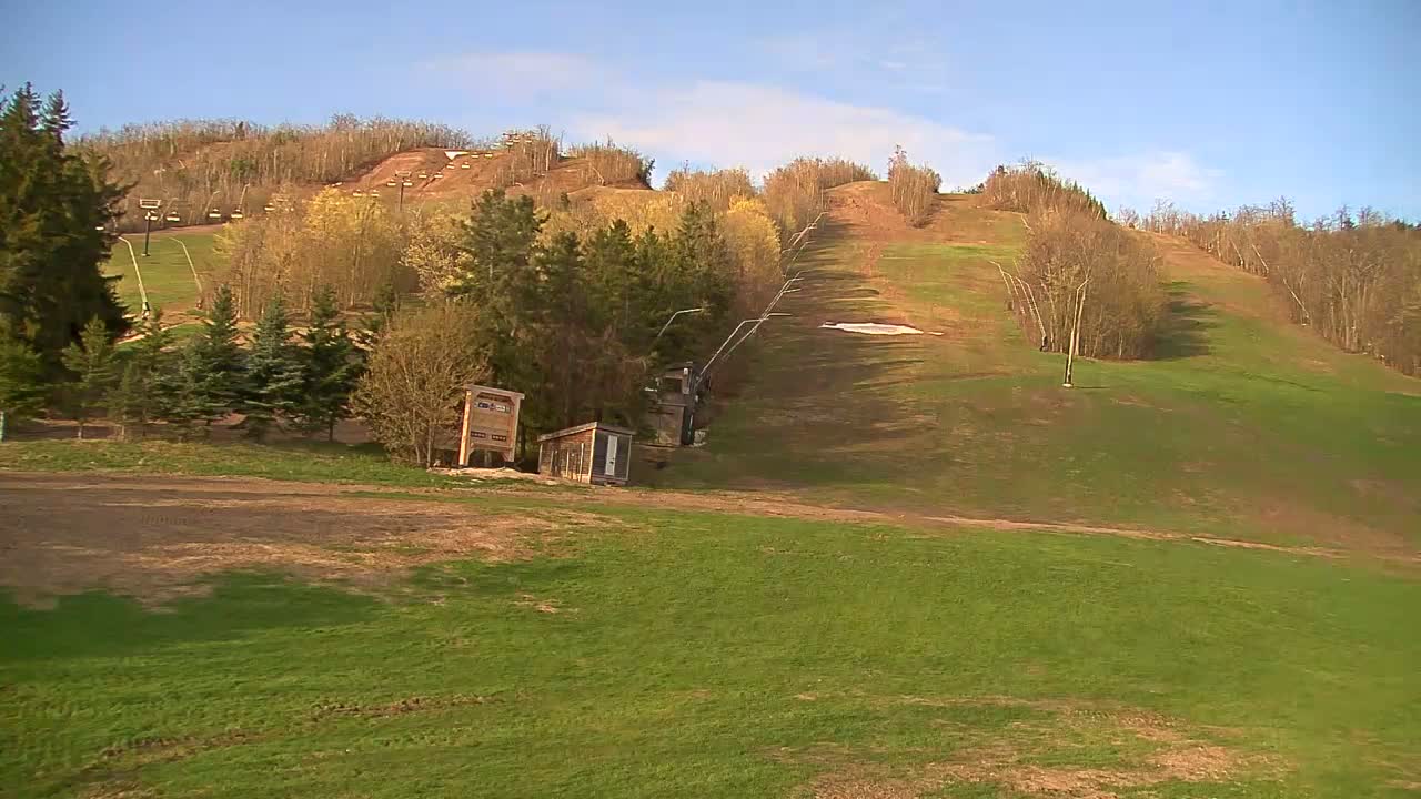 A grassy ski slope with a chairlift and small buildings is visible under a sunny sky.