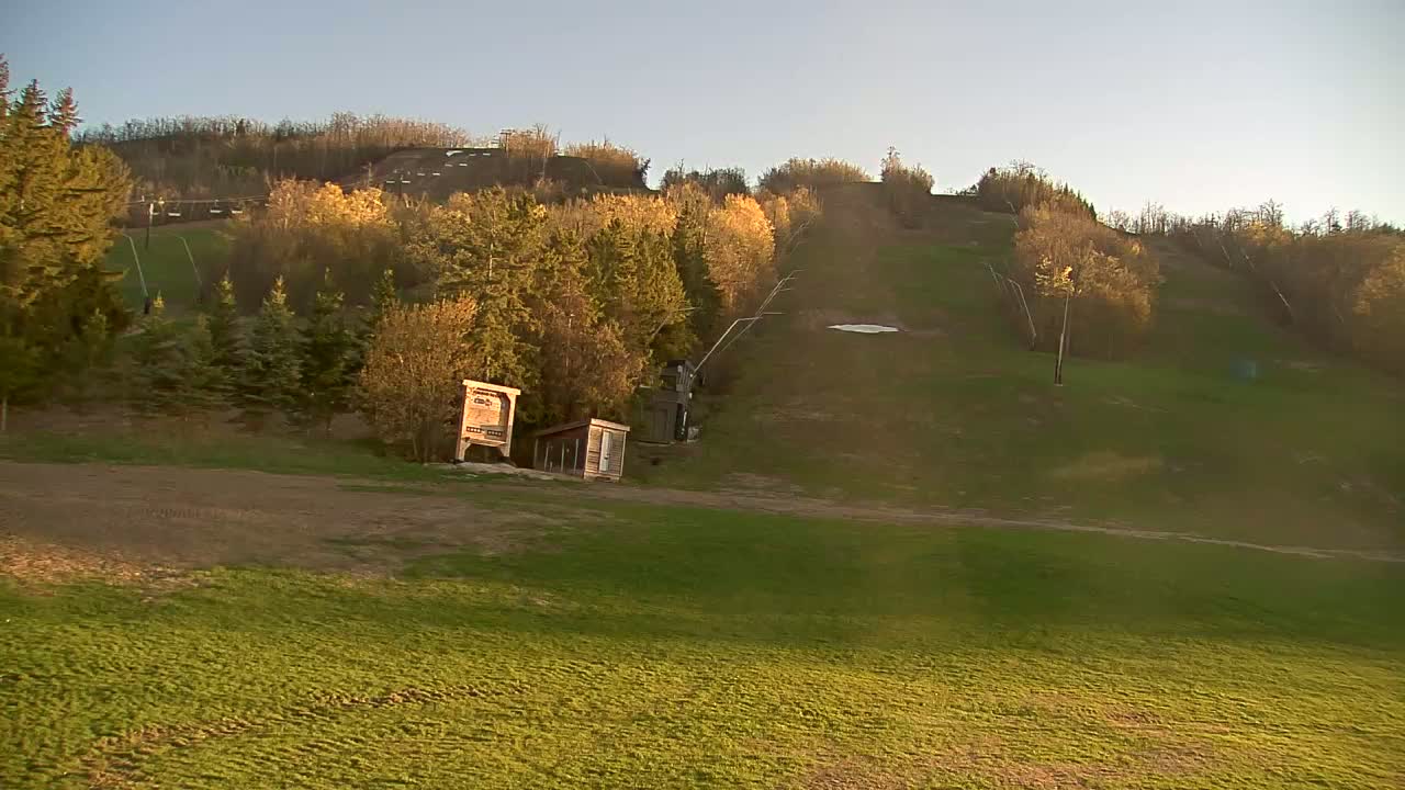 A grassy hillside with a ski lift and small buildings under a clear, sunset sky.