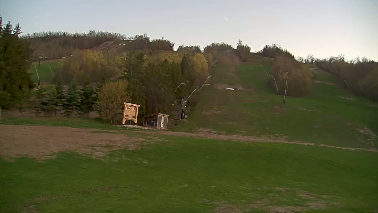 A grassy hill with a ski lift and small buildings is visible under a clear, dusky sky.