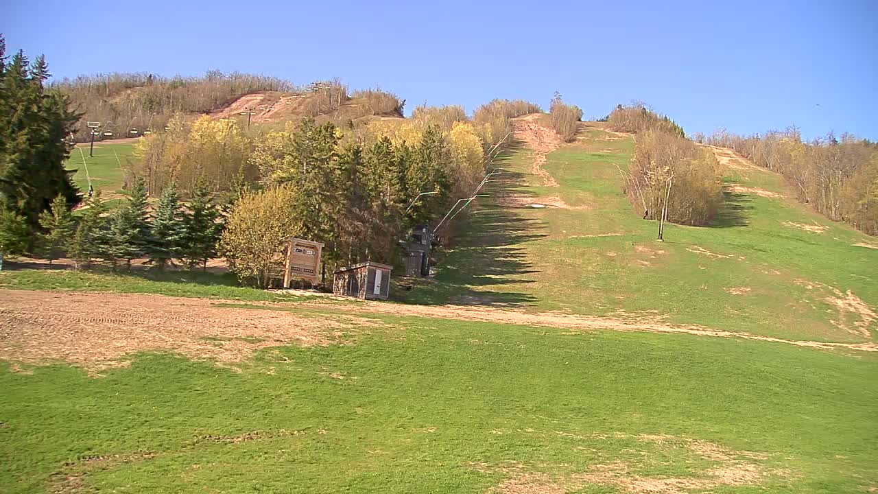 A grassy ski slope with a chairlift and small buildings is visible under a clear blue sky.
