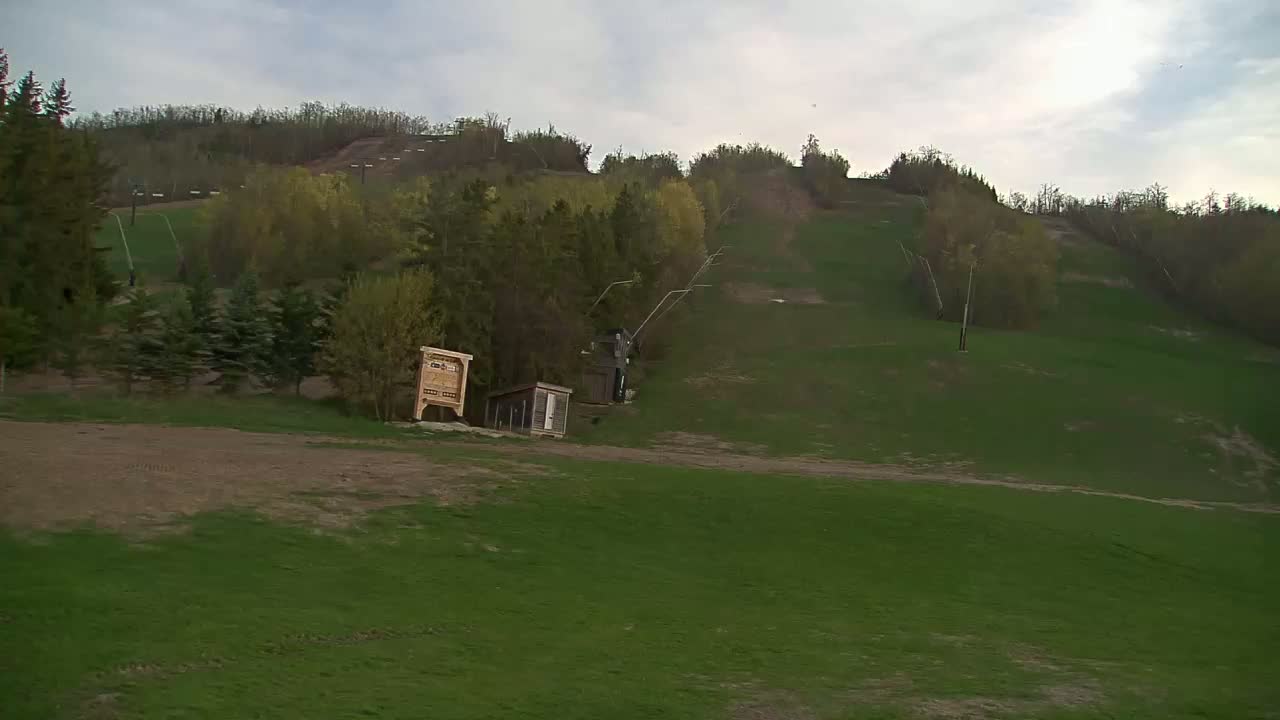 A grassy hillside with a ski lift and small buildings under a cloudy sky.