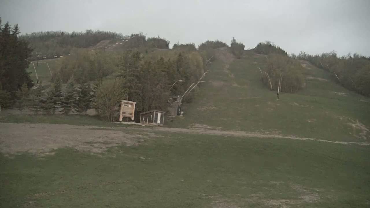 A grassy hillside with a ski lift and small buildings is visible under an overcast sky.