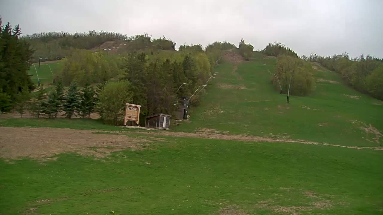 A grassy hillside with a ski lift and small buildings under an overcast sky.