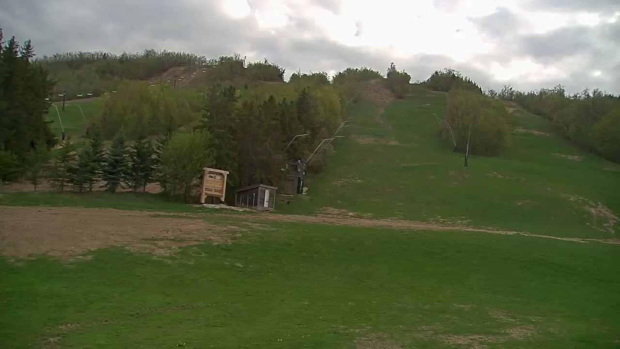 A grassy hillside with a ski lift and small structures under a cloudy sky.