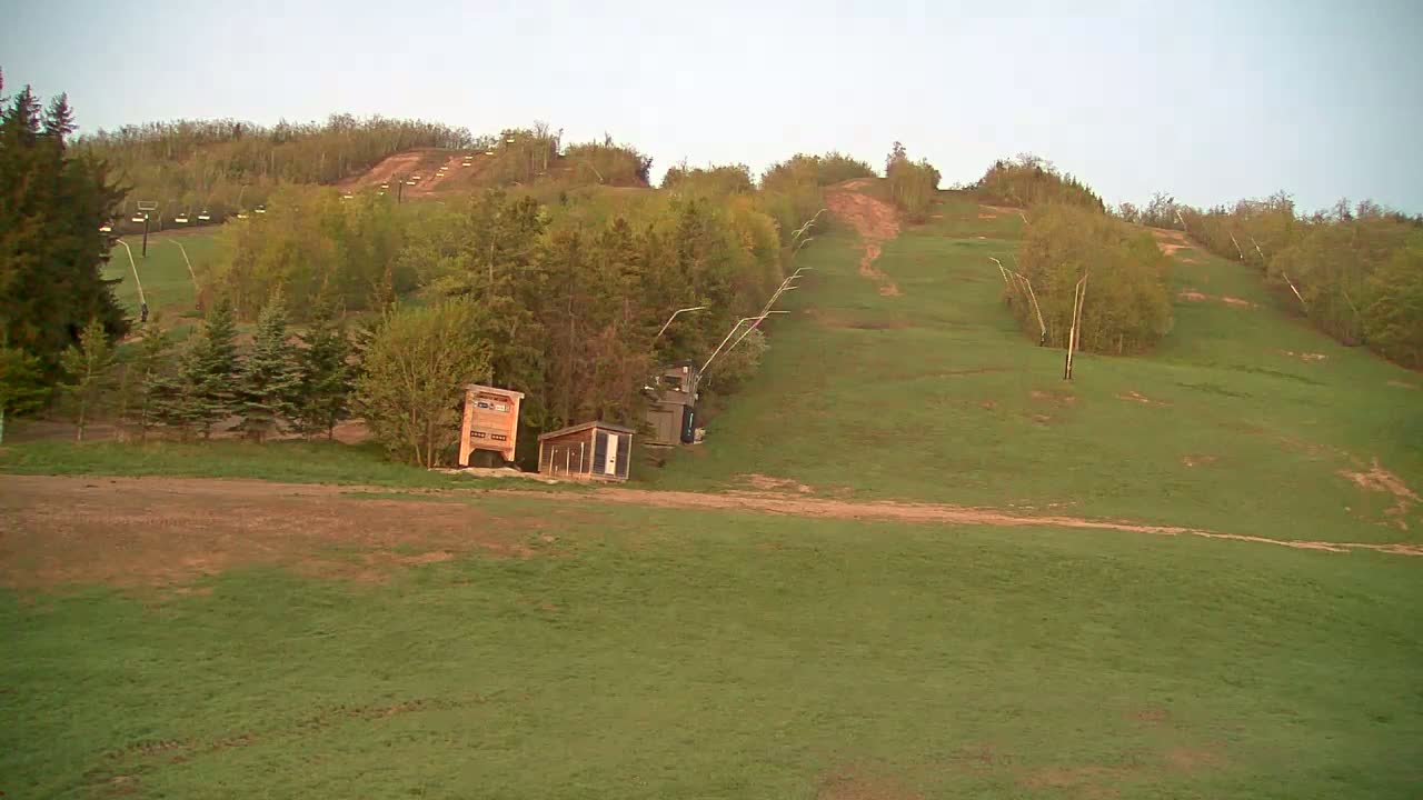 A grassy ski slope with a chairlift and small buildings is visible under a clear sky.