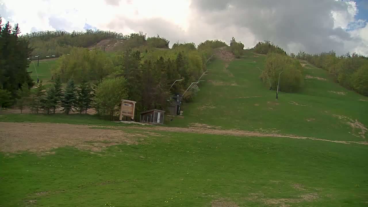 A grassy hillside with a ski lift and small buildings, under a cloudy sky.