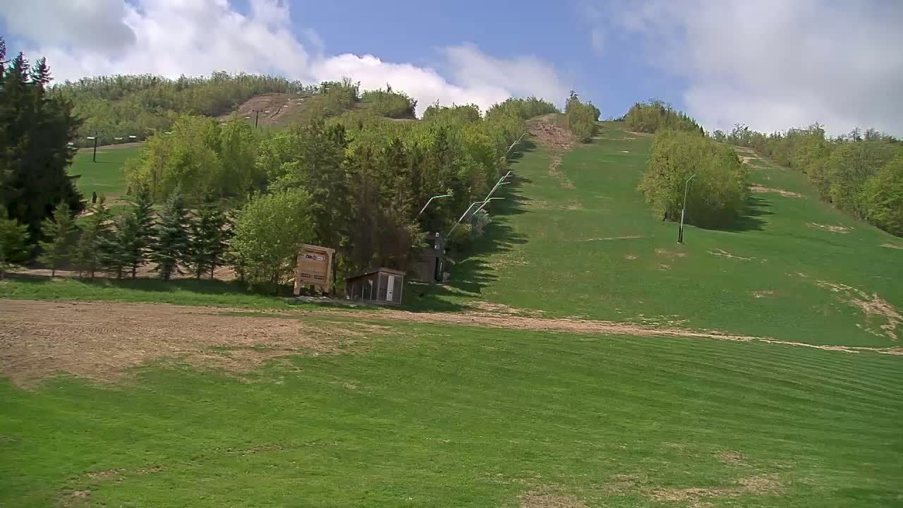 A grassy hillside, partly bare, with a ski lift visible in the background under a partly cloudy sky.