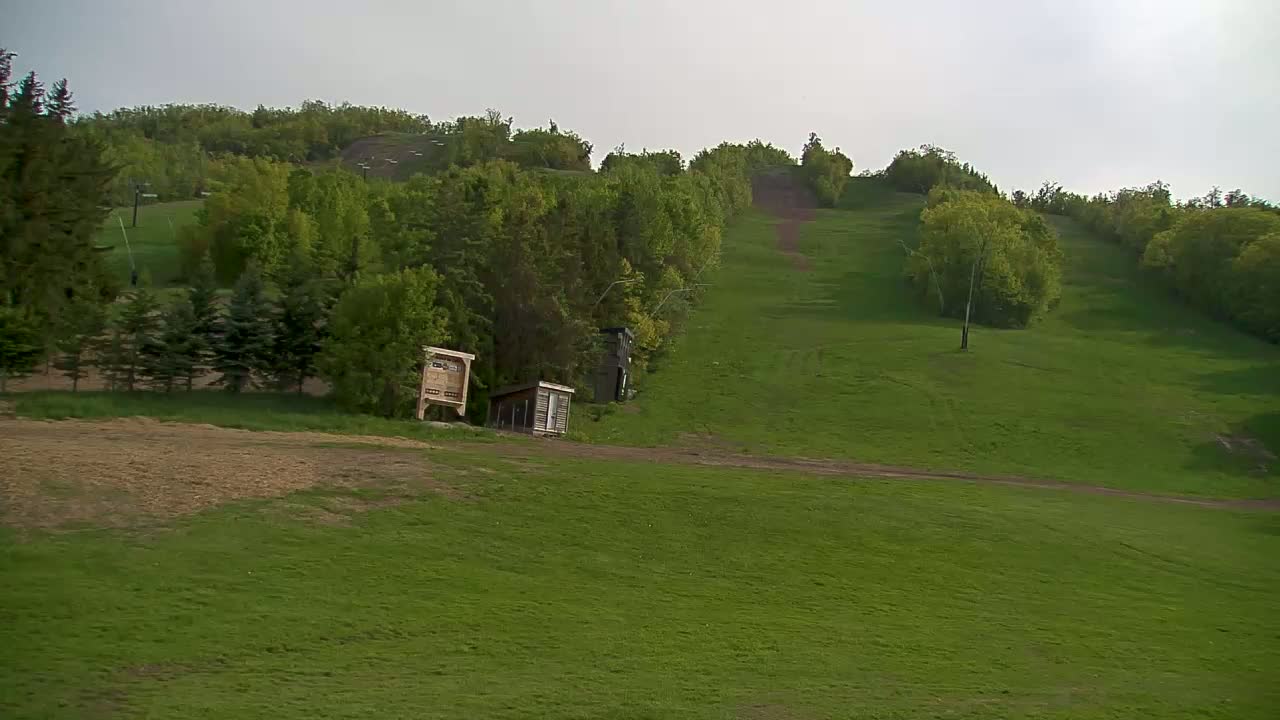A grassy hill, dotted with trees and small buildings, stretches upward under an overcast sky.