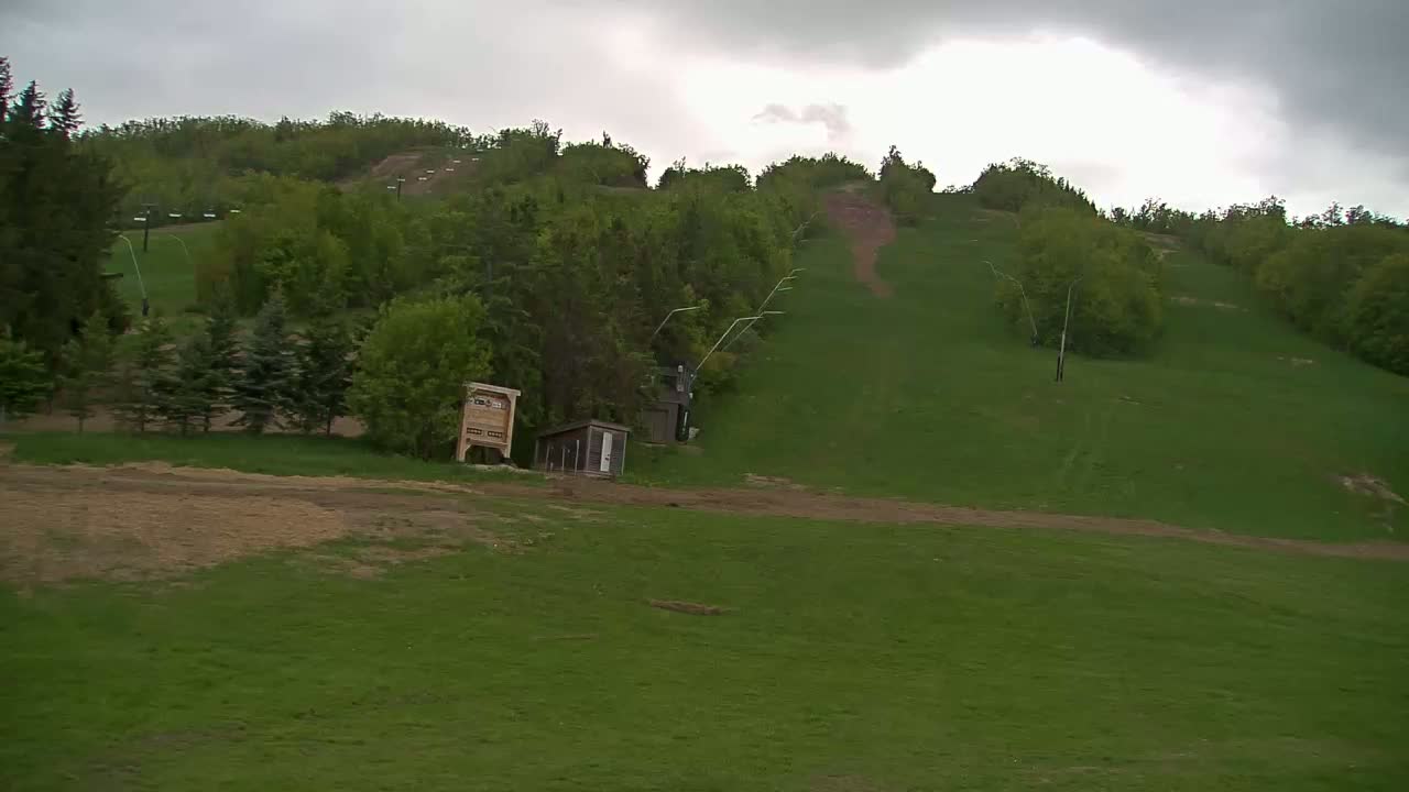 A grassy hillside with a ski lift and small buildings under an overcast sky.