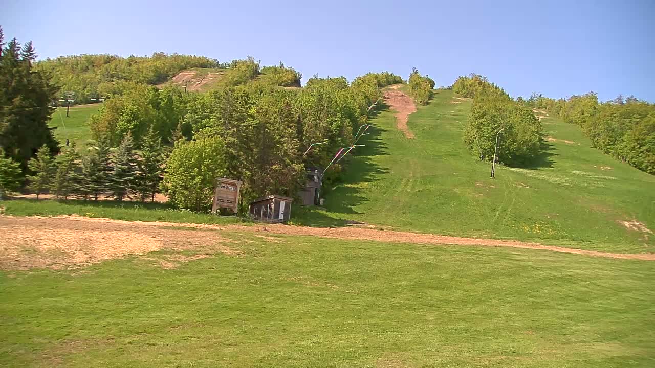 A grassy ski slope with a chairlift and small buildings is visible under a clear blue sky.