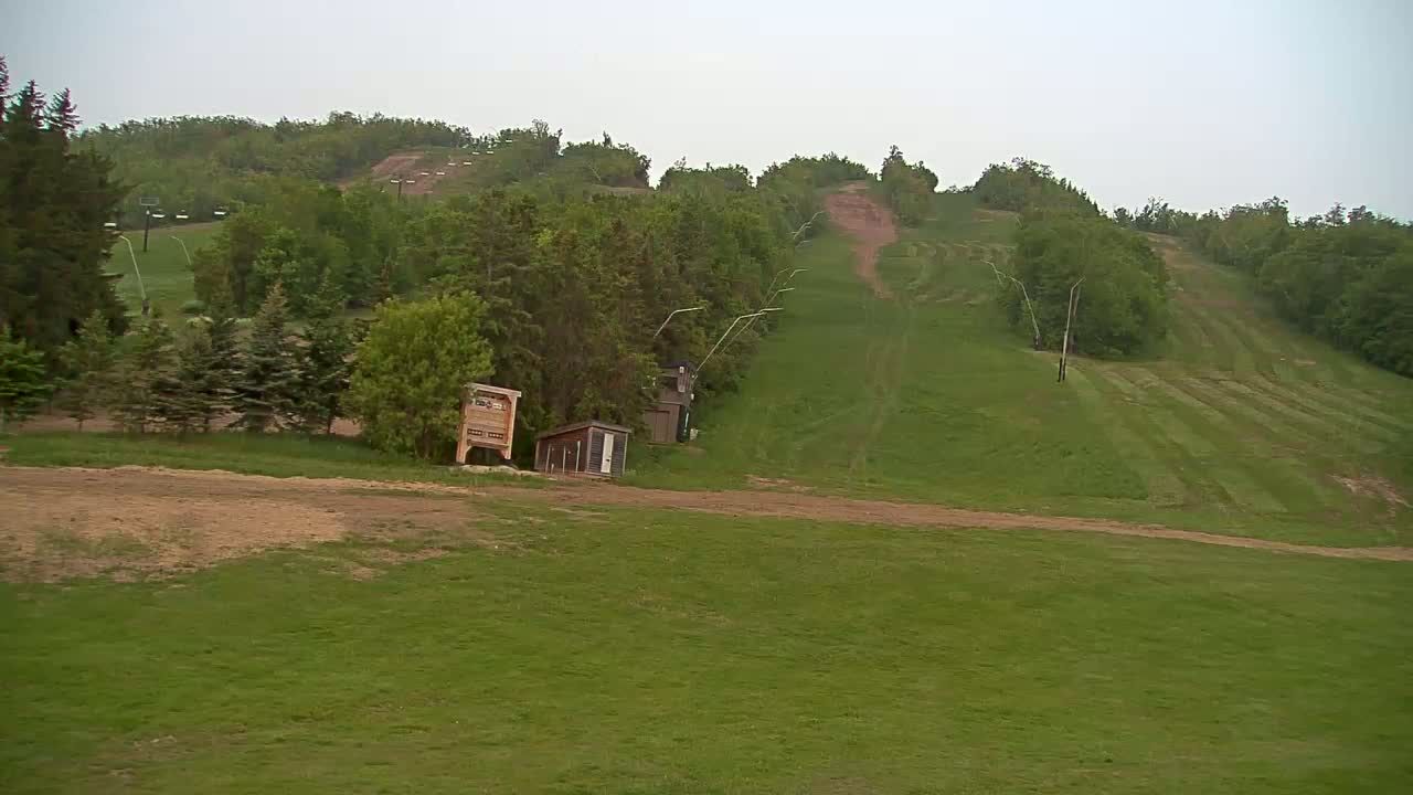 A grassy hillside with ski lifts and small structures, under an overcast sky.