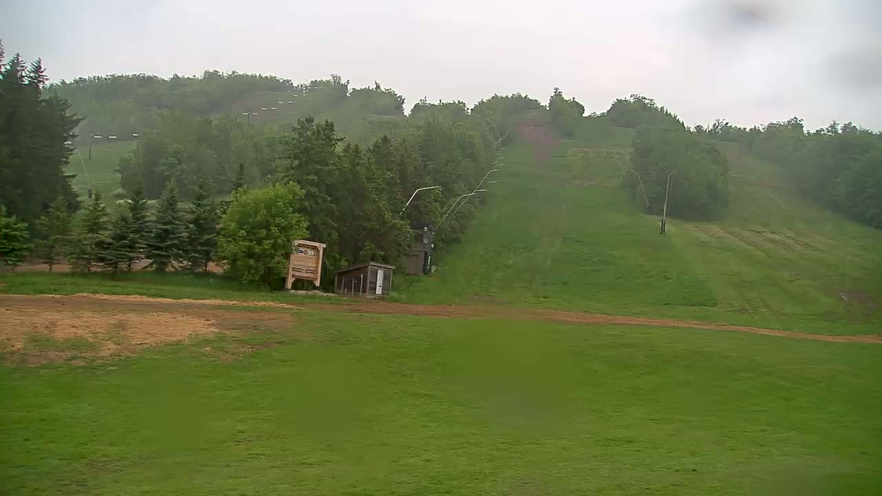 A grassy hillside with a chairlift and small buildings is visible under an overcast sky, possibly raining.
