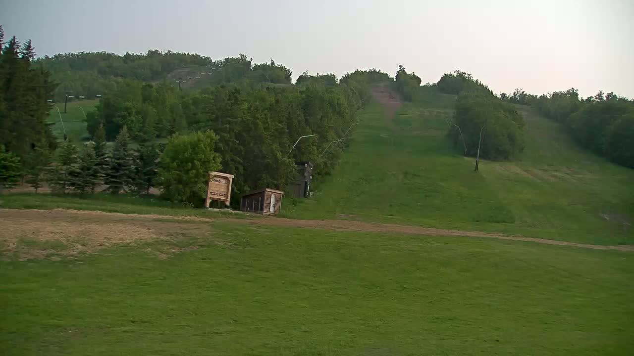 A grassy hill with a ski lift and small buildings, under an overcast sky.