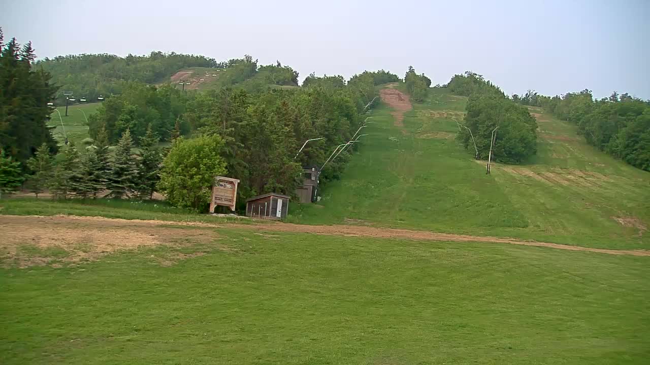 A grassy hillside with a ski lift and small buildings visible under an overcast sky.