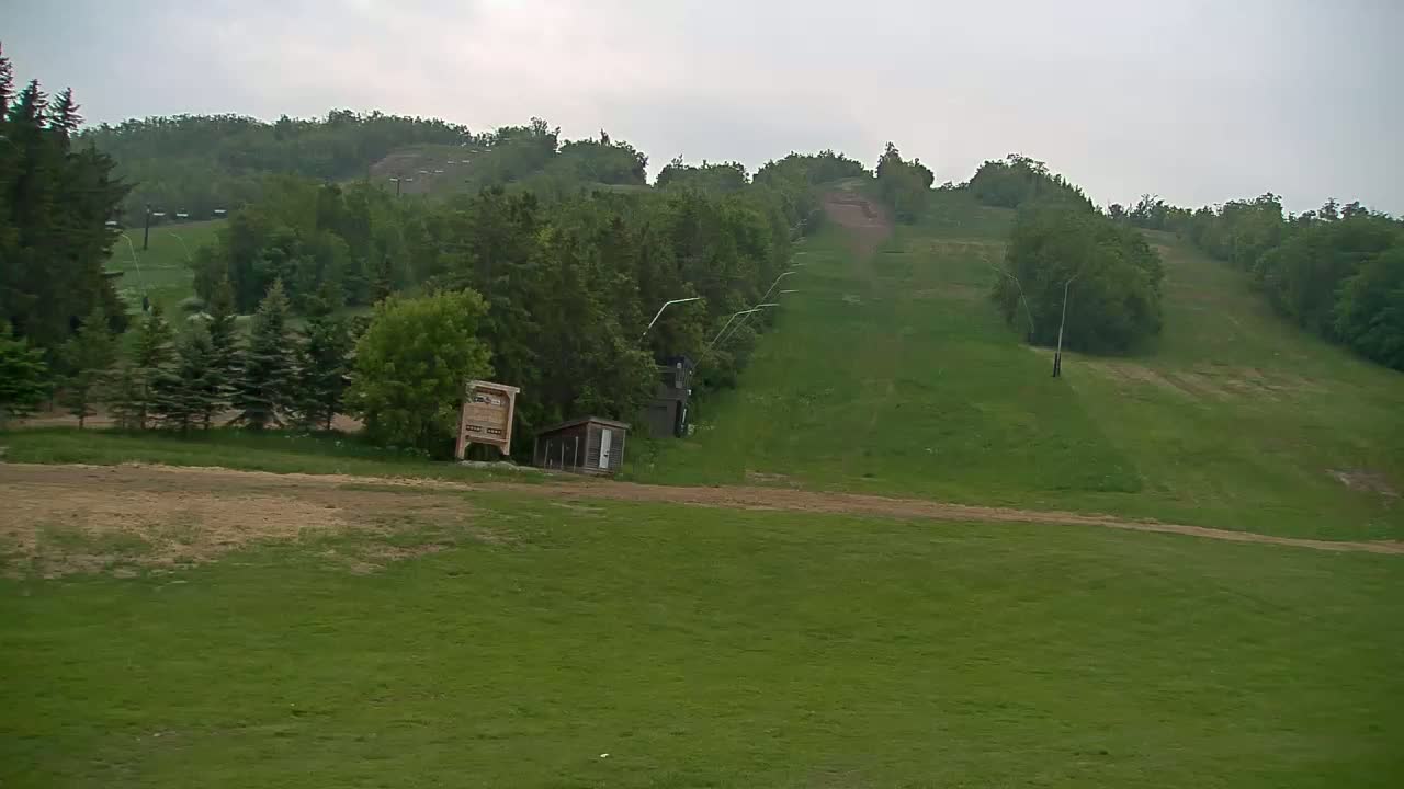 A grassy hillside with a ski lift and small buildings visible under an overcast sky.