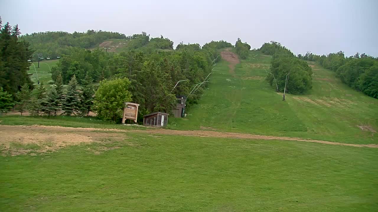 A grassy hillside with a ski lift in the background on an overcast day.