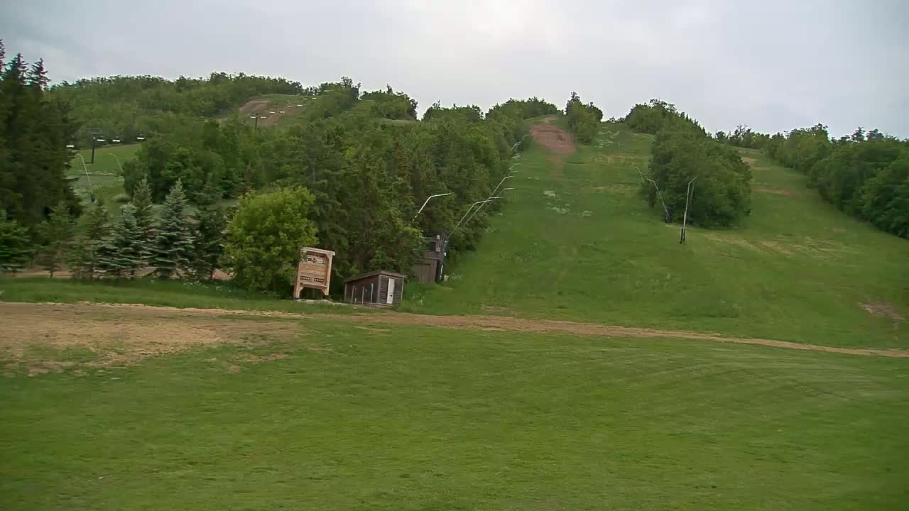A grassy hillside with a ski lift visible, under an overcast sky.