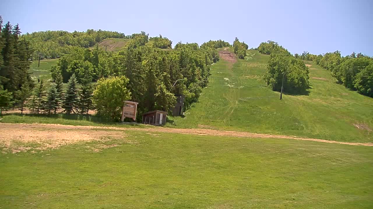 A grassy hillside covered in lush green vegetation, with a few small structures and a defunct ski lift visible on a clear, sunny day.
