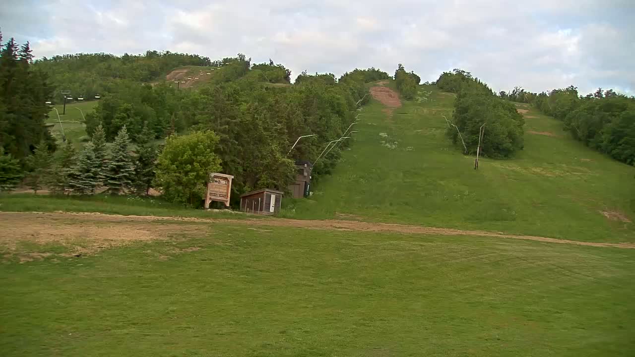 A grassy hillside with a ski lift and small buildings, under a partly cloudy sky.