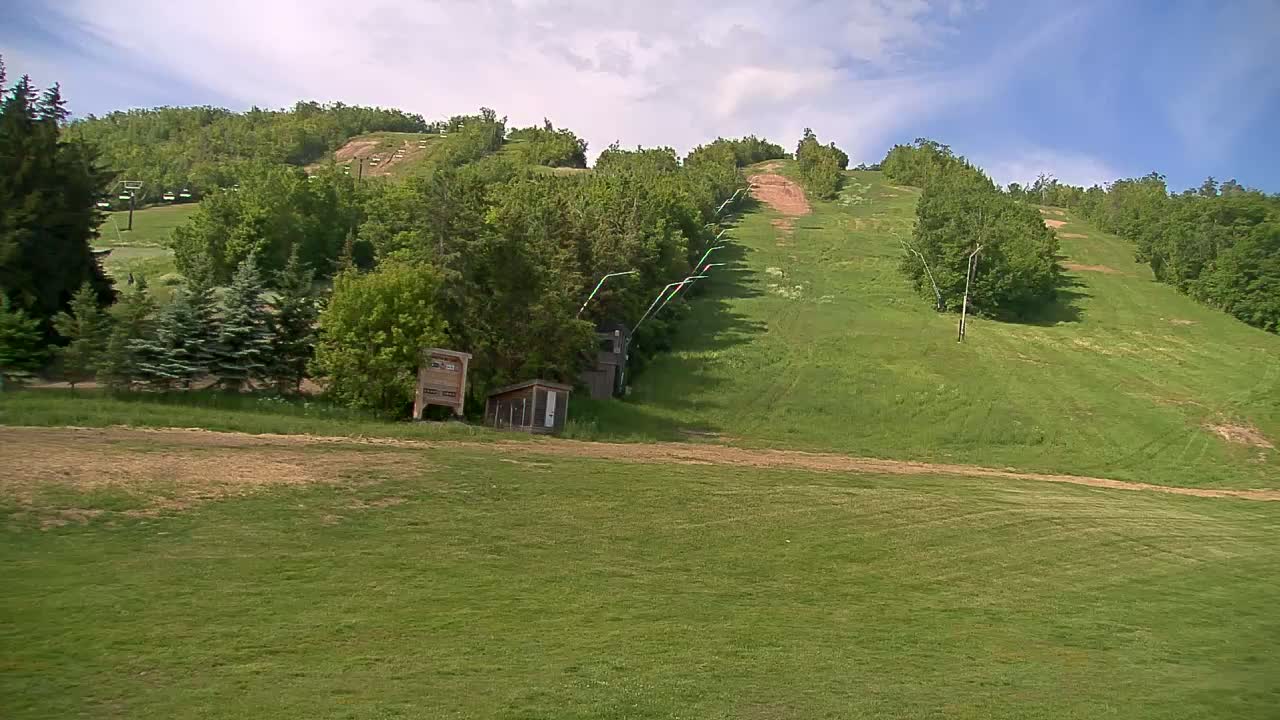 A grassy hill with a ski lift and a few small buildings under a partly cloudy sky.