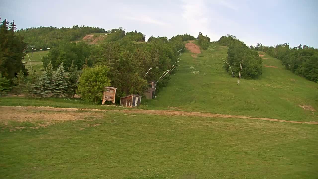 A grassy hillside with a ski lift and small buildings, under a partly cloudy sky.
