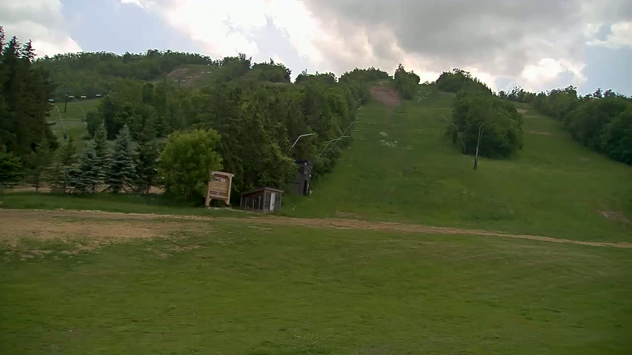 A grassy hillside with a ski lift and small buildings under a cloudy sky.